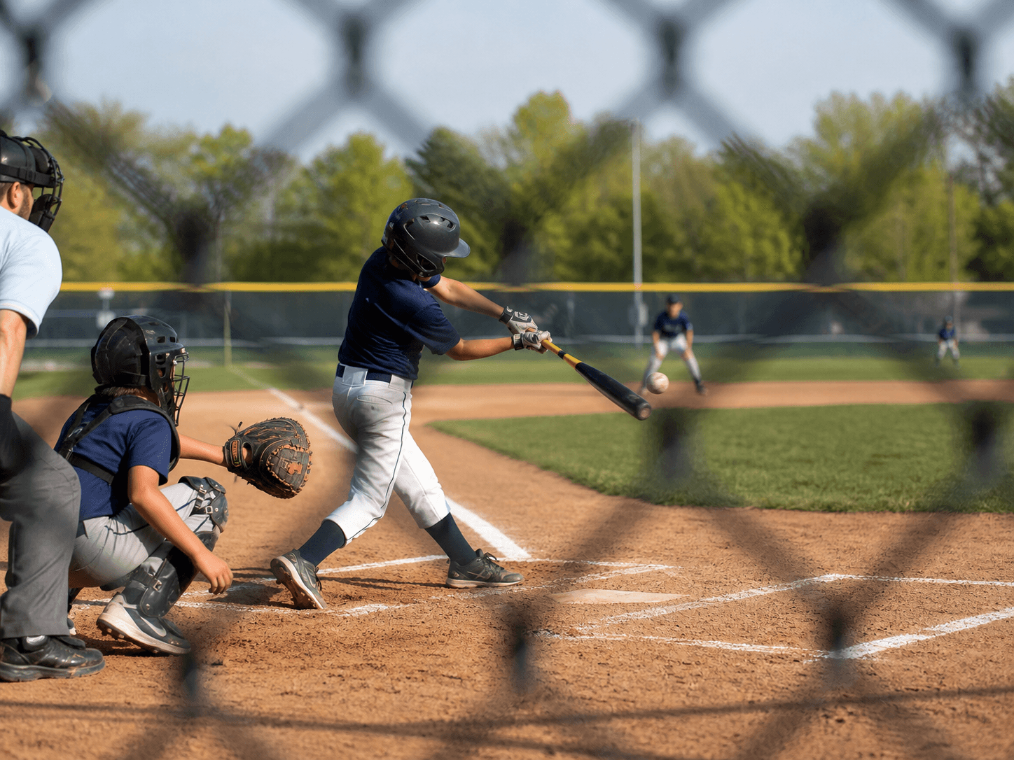 A youth baseball player swings during a game from behind a fence.
