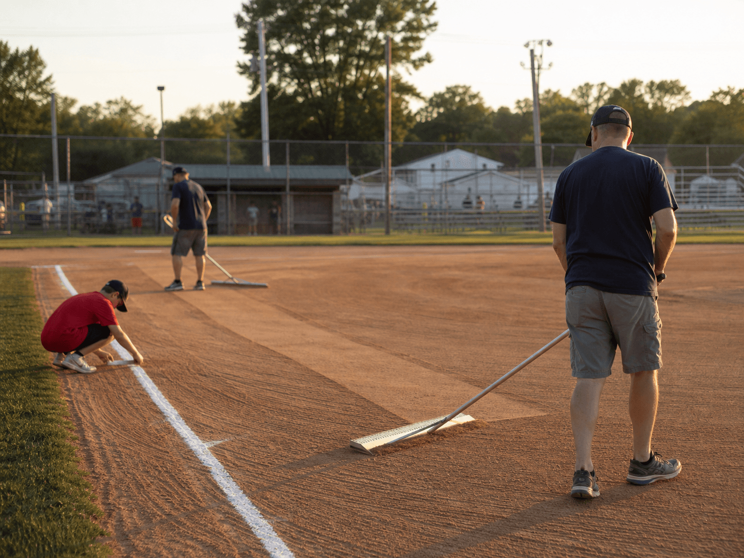 Volunteers raking and lining a baseball field before a game.